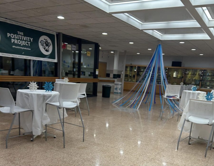 The high school foyer decorated for the winter formal with white tables and chairs and blue and purple streamers and snowflakes.