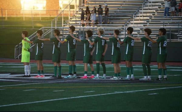 FM players dressed green line up with one arm on the shoulder of the player in front of them during the National Anthem.