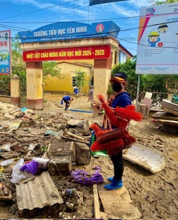 An individual poses with clean up supplies amidst debris from the hurricane in Vietnam.