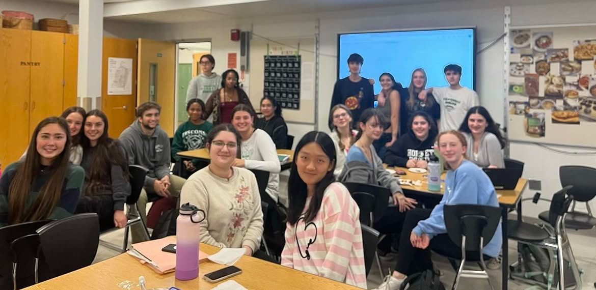 Students pose for a group photo, seated at tables with food.