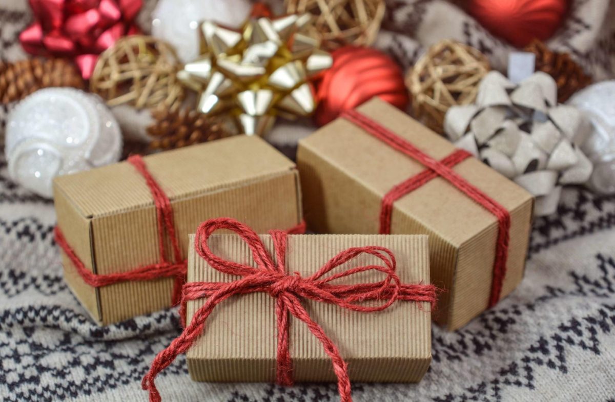 Presents are displayed, wrapped in rustic cardboard boxes and red rope ribbon. Gold bows and white and red ornaments are in the background.