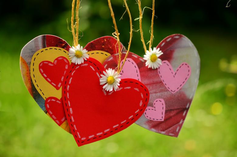 Cut out hearts in bright colors of red and pink and yellow our tied together with yellow string and daisies at the center of the hearts.