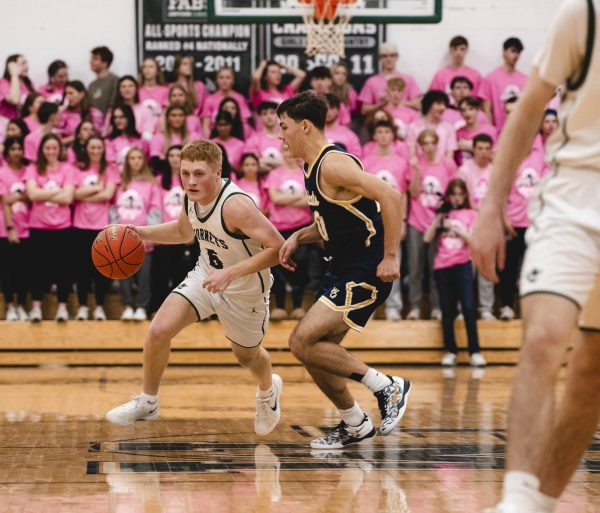 An FM player dribbles up the court with the student section in the background, all dressed in pink.