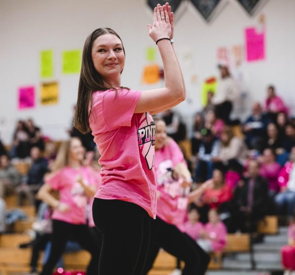 A dance team member is turned to the side smiling and clapping during the team's routine.