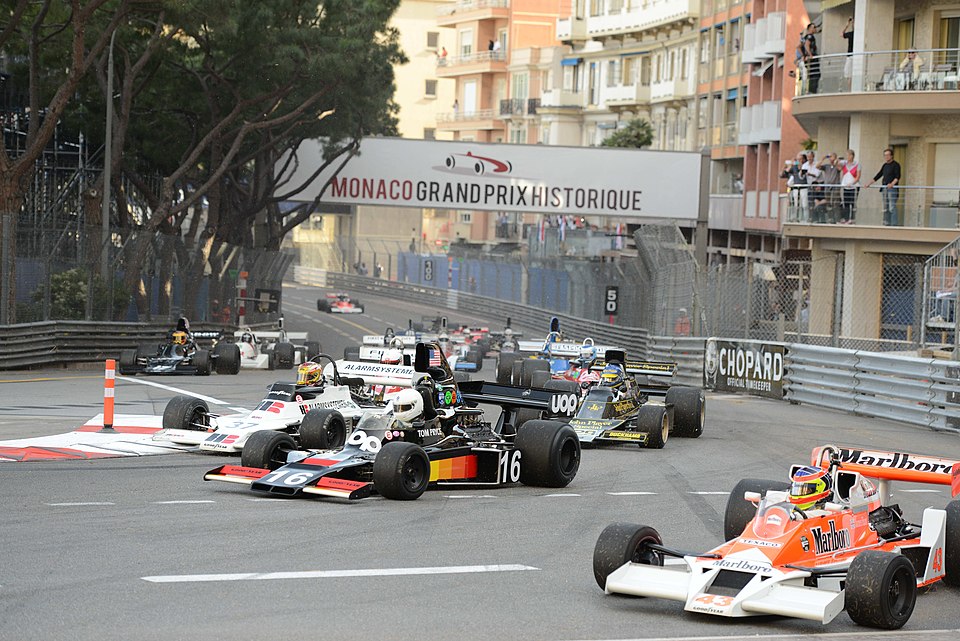 The black #16 car attempts to pass the white #37 car on a right hand curve. The Monaco Grand Prix log appears on the bridge overpass.