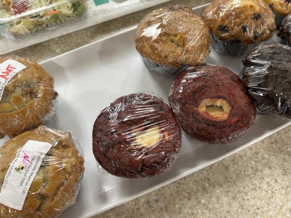 A close up of muffins wrapped in plastic. A red velvet muffin with a cream cheese center is prominent.