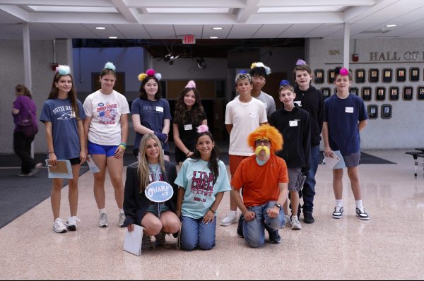 Students pose in the foyer with Lorax themed accessories. One of the leaders is dressed as the Lorax with a wig and whiskers.