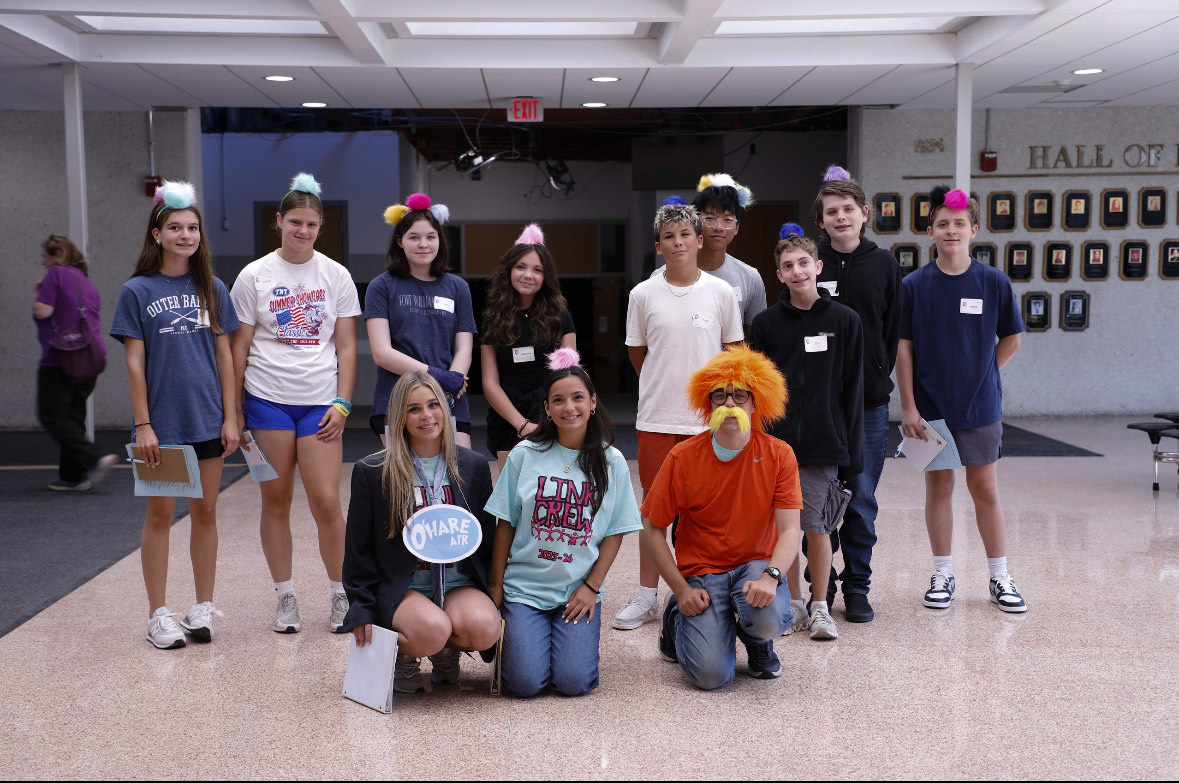 Students pose in the foyer with Lorax themed accessories. One of the leaders is dressed as the Lorax with a wig and whiskers.
