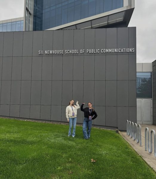 2 students posing in front of Newhouse point at the signage.