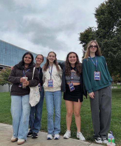 5 students, wearing their press badges, stand in front of the building.