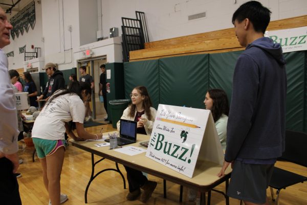 An interested student signs up to join The Buzz at the table in the gym.
