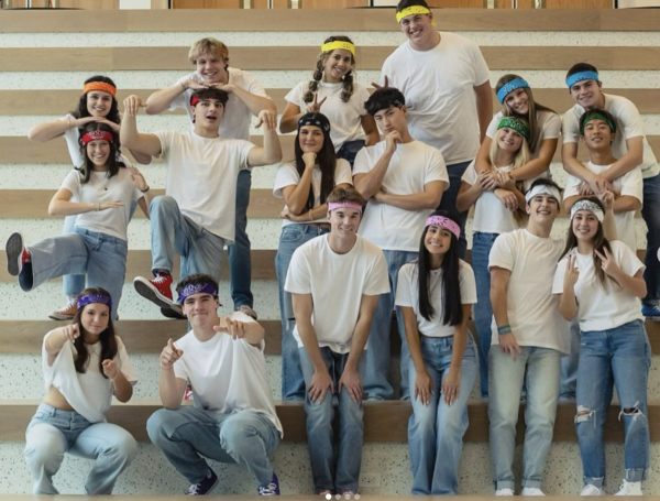 The MCs are posing on the steps of the new lower cafeteria. They are all wearing blue jeans, white t-shirts and headbands represented by their respective team's color.