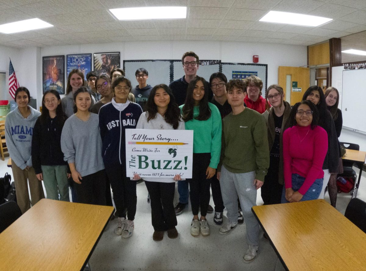 The group poses for a yearbook photo. A student in front is holding up the Buzz sign.