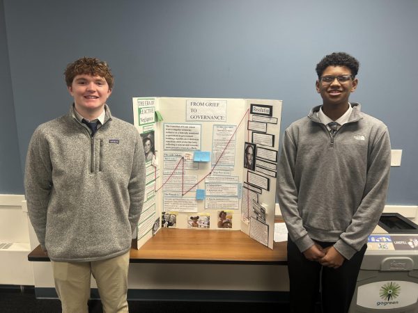 The two students stand on either side of their posterboard.