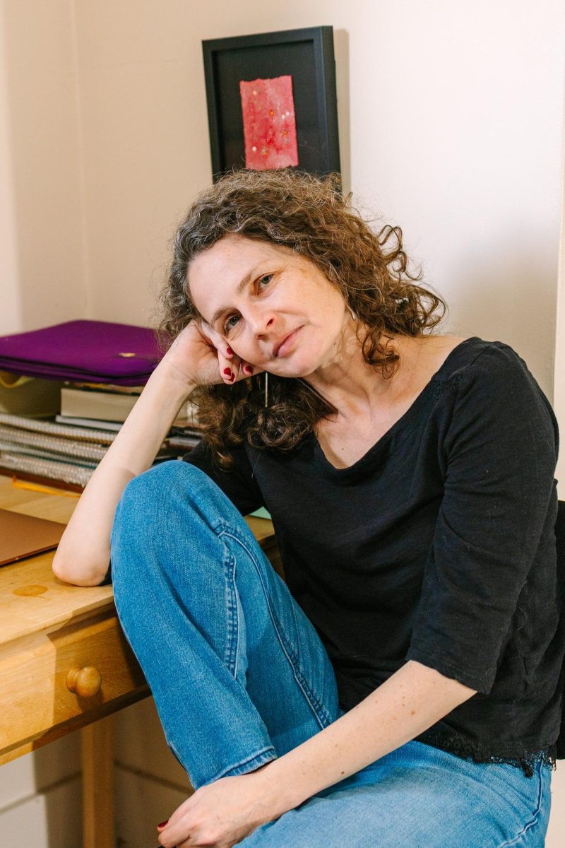 The author poses for the camera seated in a casual pose with head tilted and propped up by her hand and arm, and one leg tucked under the other on the seat of the chair.